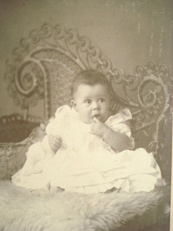Baby sitting on Victorian wicker posing chair getting its picture taken.