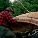 Native gentleman carving designs in the side of the birch bark canoe he is making.