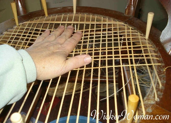 Checking proper caning tension on hole-to-hole strand caning.
