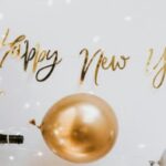 Happy New Year wishes with balloon, glitter, and champagne bottle.