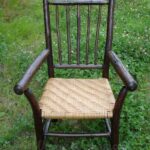 Dark colored rustic hickory arm chair with rattan reed splint seat sitting on a grassy field.