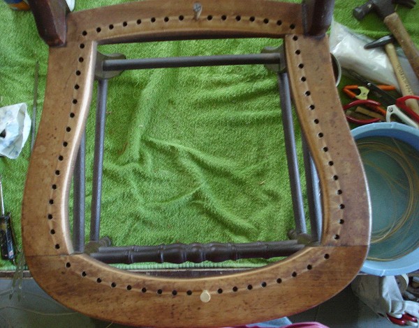 Horseshoe shaped chair frame with holes drilled around perimeter to weave the cane strands through.