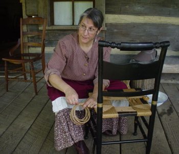 Mindy King in period attire, demonstrating how to weave a paper rush chair seat. 