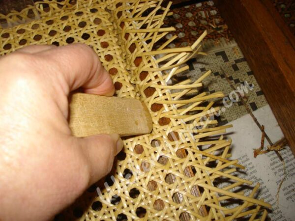 Pushing the cane webbing into the grove using a wooden chair caning wedge. 